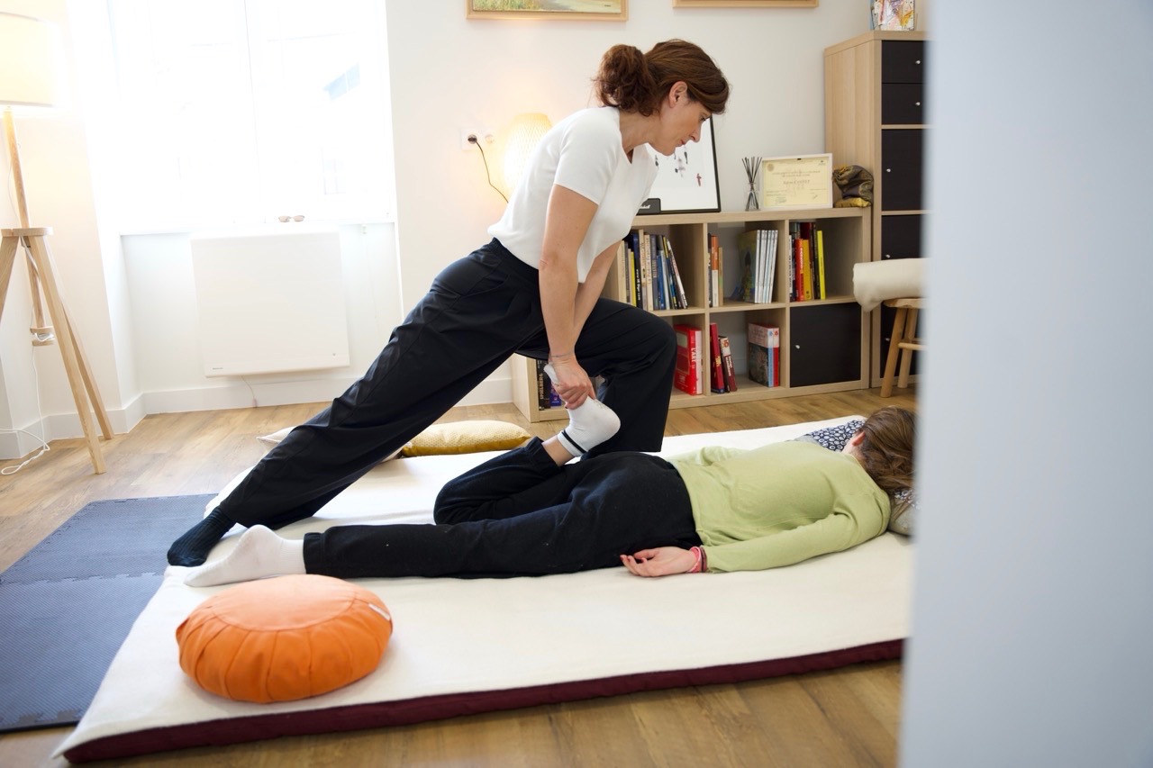 Séance au sol — Solène pratiquant un étirement sur futon, vue depuis l'entrée du cabinet
